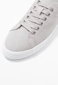 Jasnoszare płótno sneakersy z sześcioma otworami na sznurówki, białą gumową podeszwą, teksturowaną cholewką i subtelnymi detalami w szwie.