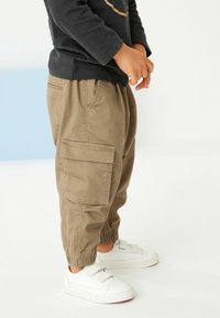 Pantalons cargo kaki avec des poignets élastiques et des poches latérales, associés à des baskets blanches avec des sangles réglables et une semelle en caoutchouc texturé.