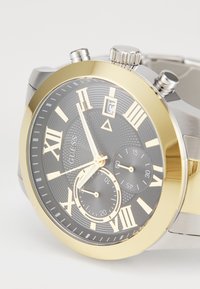 Orologio cronografo argento e dorato con quadrante nero testurizzato, numeri romani, tre sottodial e display della data. Bracciale in acciaio inossidabile.
