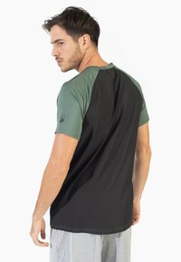 Camisa atlética negra y verde con mangas cortas, tejido texturizado, diseño ajustado y detalle del logo en el hombro izquierdo.