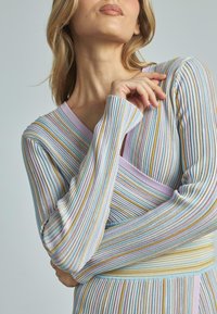Gestreiftes Langarmshirt in Pastellfarben mit gerippter Textur; zeichnet sich durch einen V-Ausschnitt und ein Wickeldesign aus, das die taillierte Silhouette betont.