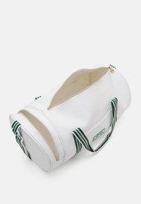 Borsa da viaggio sintetica bianca con manici a strisce verdi e bianche, chiusura con zip e un ampio scomparto. Presenta una piccola tasca frontale.