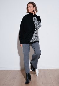 Pulover negru cu guler înalt, cu manșon din imprimeu leopardo, asortat cu pantaloni gri cu picioare largi și cizme negre cu toc. Textură fină și stil casual.