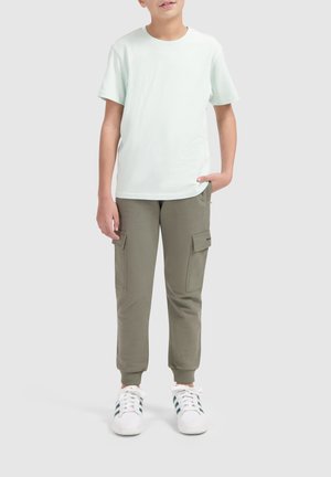 Lichtgroene t-shirt met korte mouwen, gecombineerd met olijfgroene cargobroek met twee grote zakken en witte sneakers met groene strepen.
