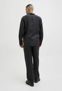 Chemise noire en lin avec une coupe décontractée, manches longues et poignets à boutons, associée à un pantalon ample assorti et des chaussures foncées.