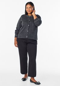 Sivani pleteni kardigan s okruglim izrezom, zatvaranjem na gumbe i perlicama duž ovratnika. Uparen s crnim ravnim hlačama i balerinkama.