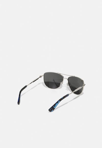 Metāla rāmīša saulesbrilles ar pelēkiem stikliem, kas izceļas ar elegantu, stūrainu dizainu. Tempļi ir melni ar zilu akcentu un teksturētu apdari.