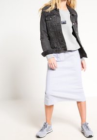 Veste en denim noire, sweat-shirt gris avec un patch, jupe midi rayée et chaussures de sport grises. Tenue décontractée superposée avec des textures.