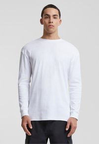 Hvit langermet T-skjorte med rund hals, laget av bomull med en glatt tekstur, tettsittende snitt og standard mansjetter. Enkel, ensfarget design.