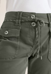 Gros plan sur un pantalon cargo vert foncé avec une poche rabat boutonnée et une ceinture en tissu nouée en un nœud à la taille.
