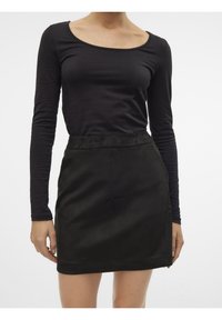 Chemise noire à manches longues avec un décolleté dégagé, associée à une jupe patineuse en suède noir, présentant une texture lisse et des poches latérales sur les coutures.