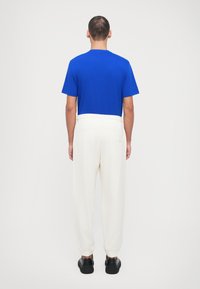 T-shirt bleu à manches courtes associé à un pantalon de jogging blanc et des baskets noires. Le t-shirt a un col rond ; le pantalon présente une taille élastique.