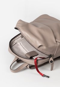 Zaino in pelle beige con apertura a zip. L'interno presenta un motivo geometrico con un anello accentato in rosso e diversi scomparti per la stivaggio.