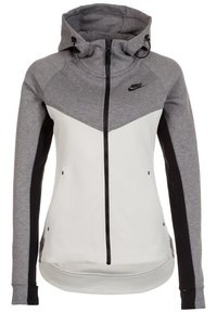 Nike mikina s kapucí s šedobílo blokovým designem, plným zipem a jemně strukturovaným materiálem. Obsahuje nastavitelnou kapuci se šňůrkou.