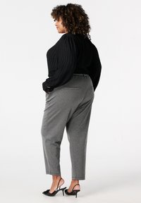 Zwarte geribbelde trui met pofmouwen, gecombineerd met grijze geblokte broeken en zwarte open-toed hakken, die een ontspannen silhouet toont.