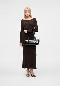 Brun ribbestrikket kjole med lange ermer, midtkalvlengde, kombinert med en svart rektangulær håndveske og svarte sandaler med høye hæler og stropper.
