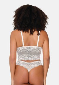 Bralette in pizzo e slip coordinati in morbido crema; presenta un motivo floreale, bordi scallop e spalline sottili regolabili.