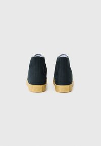 Adidași negri din canvas, cu vârf înalt, pată rotundă neagră, căptușeală albă și tălpi din cauciuc cu textură, având un finisaj texturat și cusături întărite.