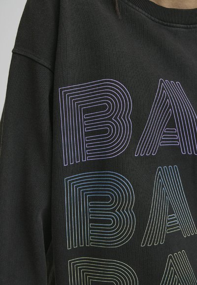 Svart sweatshirt med flerfargede, konturerte bokstaver som staver "BAB" i varierende tykkelse, som viser en teksturert stoff med rund hals.