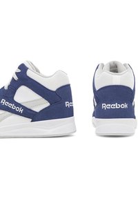 Balts un tumši zili Reebok sporta apavi, parādot sānu un aizmugures skatus uz balta fona.