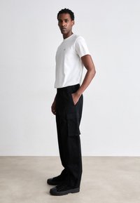 Hvid bomuld t-shirt med et lille logo, parret med sorte cargo-bukser med sidelommer og elastik i livet, samt sorte sneakers.