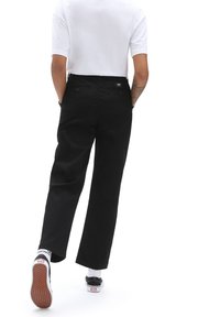Černé kalhoty rovného střihu s vysokým pasem, zadními kapsami a detailem s etiketou. Kombinované s bílou košilí s krátkým rukávem a černými botami.