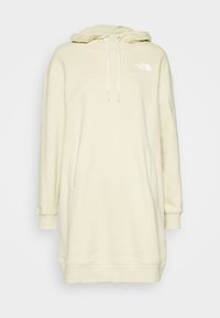 Ljus krämfärgad hoodieklänning i mjukt tyg, med en känguruficka, långa ärmar och snoddar på huvan. Logotypen visas på bröstet.