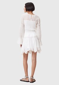 White dress with a smocked bodice and long, flared sleeves; layered skirt with a hemline that dips at the back; paired with flat sandals.