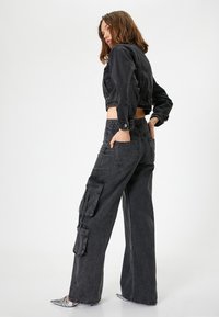 Svart denimjacka med kort ärm, kombinerad med vida cargobyxor. Byxorna har stora sidofickor och en avslappnad passform. Blanka silverfärgade skor.