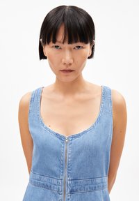 Helles blaues Denimkleid mit Rundhalsausschnitt und einem Frontreißverschluss. Mit breiten Trägern und einer taillierten Passform. Glatte Textur.