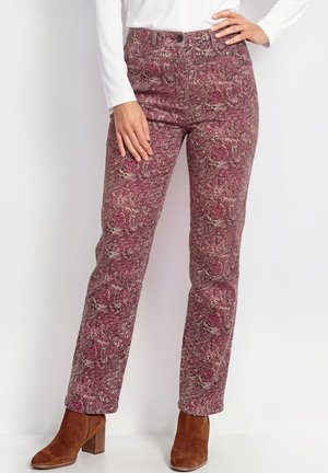 Donna che indossa pantaloni aderenti a vita alta con fantasia floreale rosa e grigia, stivaletti in pelle scamosciata marrone con tacco e una maglietta bianca a maniche lunghe.