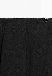 Cintura in tessuto nero strutturato con chiusura laterale con bottone e dettaglio passante per cintura su pantaloni o gonna.