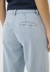 Vaaleansiniset denimit, joissa on rento leikkaus, sisältävät kaksi takataskua ja hienovaraisia ompeluulaattoja. Tasainen rakenne, klassinen viisitaskumalli.