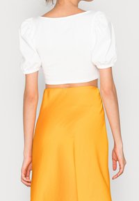Bílé vykrojené tričko s nabíranými rukávy, zkombinované s volnou oranžovou sukní. Hladká textura a minimalistický design se čtvercovým výstřihem na zádech.