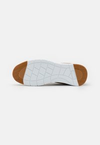White sneaker sole with a textured grip pattern. Features a gum rubber accent. Rounded shape with molded lines for flexibility.