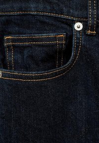 La tela de mezclilla oscura presenta un bolsillo trasero detallado con costuras naranjas en contraste y un pequeño remache de metal, realzando la durabilidad y el diseño.