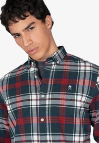 Camisa de cuadros en rojo, verde y blanco con cuello; presenta un pequeño logo en el pecho y un diseño de ajuste estándar.