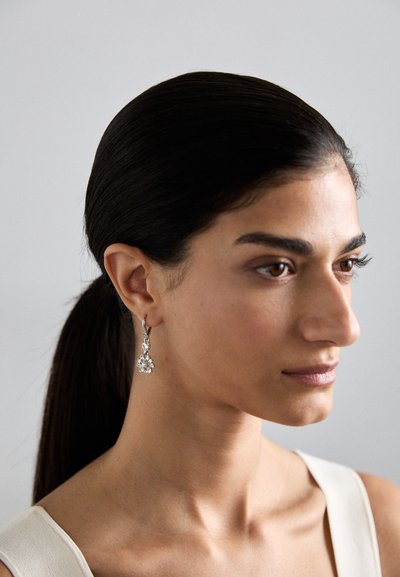 Silberne Tropfohrringe mit klaren, blütenförmigen Akzenten, die über filigrane Details und ein poliertes Finish verfügen. Das minimalistische Design unterstreicht die Eleganz.
