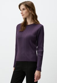 Paarse ribbeltrui met lange mouwen en ronde hals, gemaakt van een gladde, gestructureerde stof. Gecombineerd met zwarte broek.