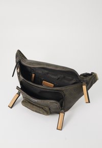 Sac bandoulière en toile vert olive avec plusieurs compartiments zippés, des poignées texturées et des accents en cuir, doté d'une doublure intérieure avec logo.