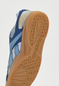 Reebok tenisice s teksturiranim plavim i bež gornjim materijalima, s gumiranim potplatom koji ima uzorak za prianjanje.
