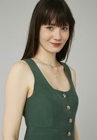 Robe en lin vert avec un corsage ajusté, de larges bretelles, un bouton sur le devant et de petites poches latérales. Tissu texturé avec une finition mate.