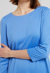 Lichtblauw langemouwtop met een ronde halslijn, zachte textuur en subtiele gradient die naar een donkerdere tint aan de onderkant vervaagt.