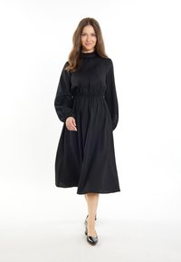 Rochie neagră cu mânecă lungă, talie ajustată, fustă lejeră și decolteu volantat. Țesătură netedă cu detalii subtile la piept.