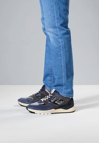 Marineblaue und graue Sportschuhe aus einer Kombination von Mesh- und Wildledermaterialien, mit weißen Schnürsenkeln und einer strukturierten Sohlendetail.