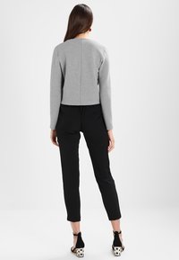 Szary skrócony sweter z teksturowanym wykończeniem, zestawiony z czarnymi dopasowanymi spodniami i czarnymi szpilkami z akcentem w kropki.