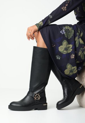 Bottes noires en cuir montantes avec un accent logo doré, bout rond et talon épais. Texture lisse avec une silhouette élégante.