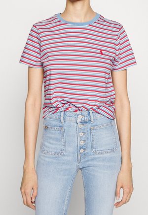 Osoba ubrana w krótki rękaw koszulki w czerwono-biało-niebieskie paski, włożoną do wysokowaterowanych jasnoniebieskich jeansów zapinanych na guziki.