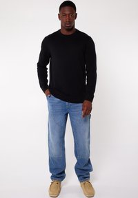 Black sweater, loose-fit light blue jeans with large pockets, and tan shoes. Materials include cotton and denim with a casual design.