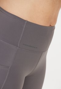 Grå højtaljede leggings lavet af strækbart stof med flade sømme og et lille "ENDURANCE" logo på livkosten.